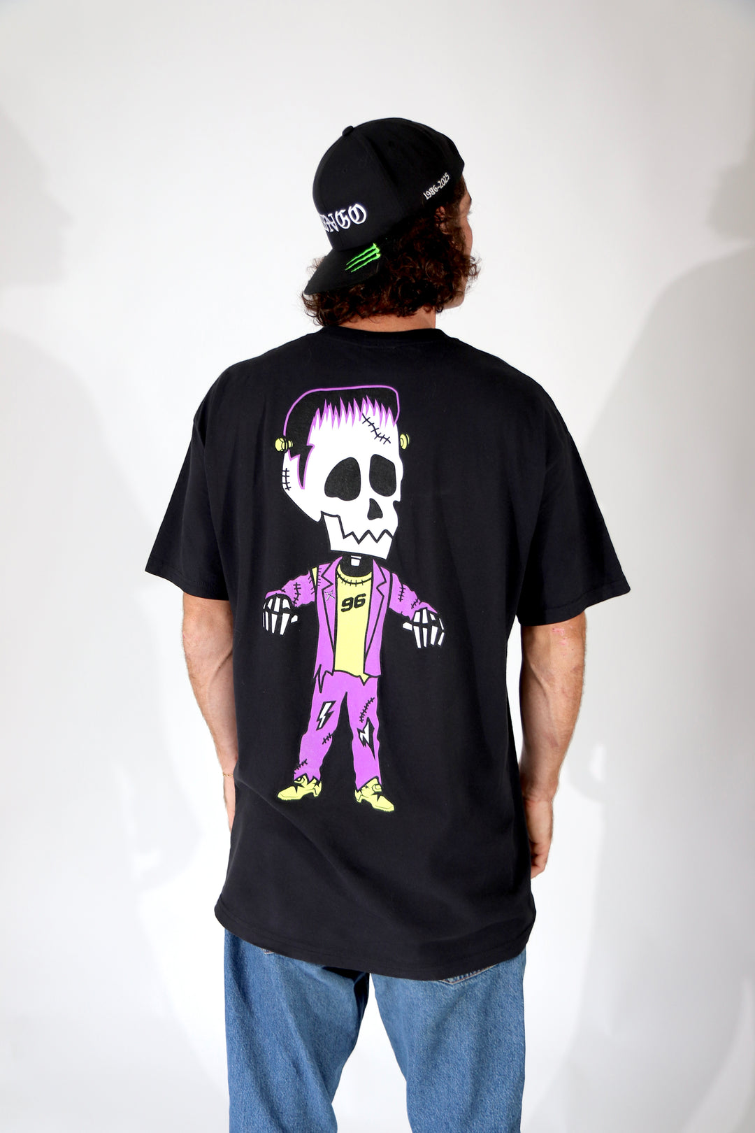 Person wearing a black t-shirt with a colorful skeleton design on the back, standing against a white background. Halloween frankenstein