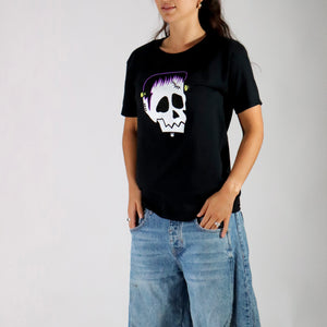 Person wearing a black t-shirt with a skull design and blue jeans on a plain background