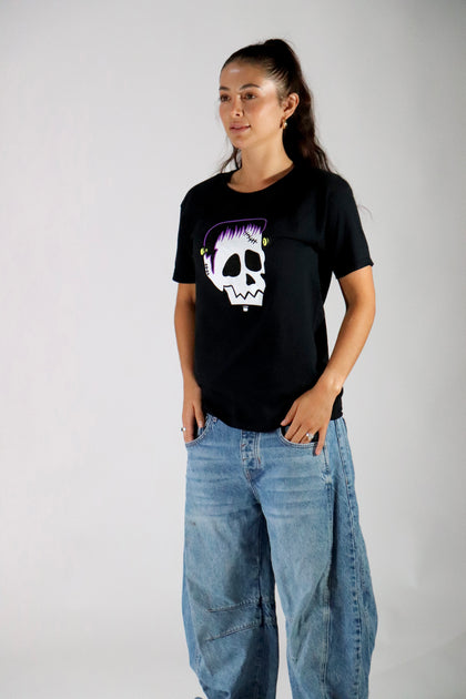 Person wearing a black t-shirt with a skull design and blue jeans on a plain background