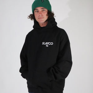 Axell Hodges wearing a black hoodie with  slayco text and a green beanie on a light gray background