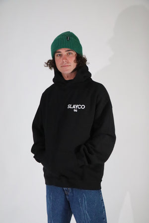Axell Hodges wearing a black hoodie with  slayco text and a green beanie on a light gray background